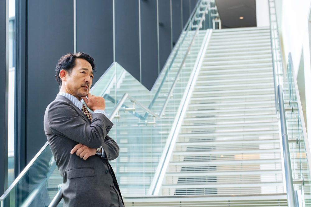 オフィスの階段前で顎に手を当てて思考する経営者