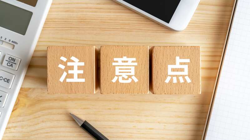 電卓やスマートフォンとペンが並ぶデスクと、「注意点」と書かれた木製ブロック